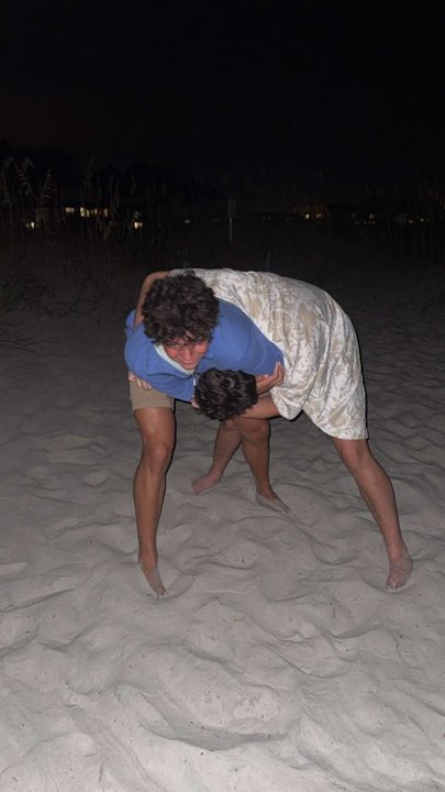 Ayden and Alex wrestling on the sand at night.